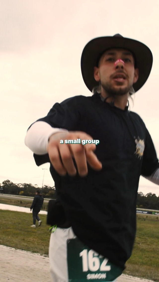 Runner in a cowboy hat pointing at the camera mid race
